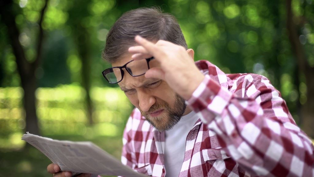 גבר מרים משקפיים ומתקשה לקרוא עיתון בפארק